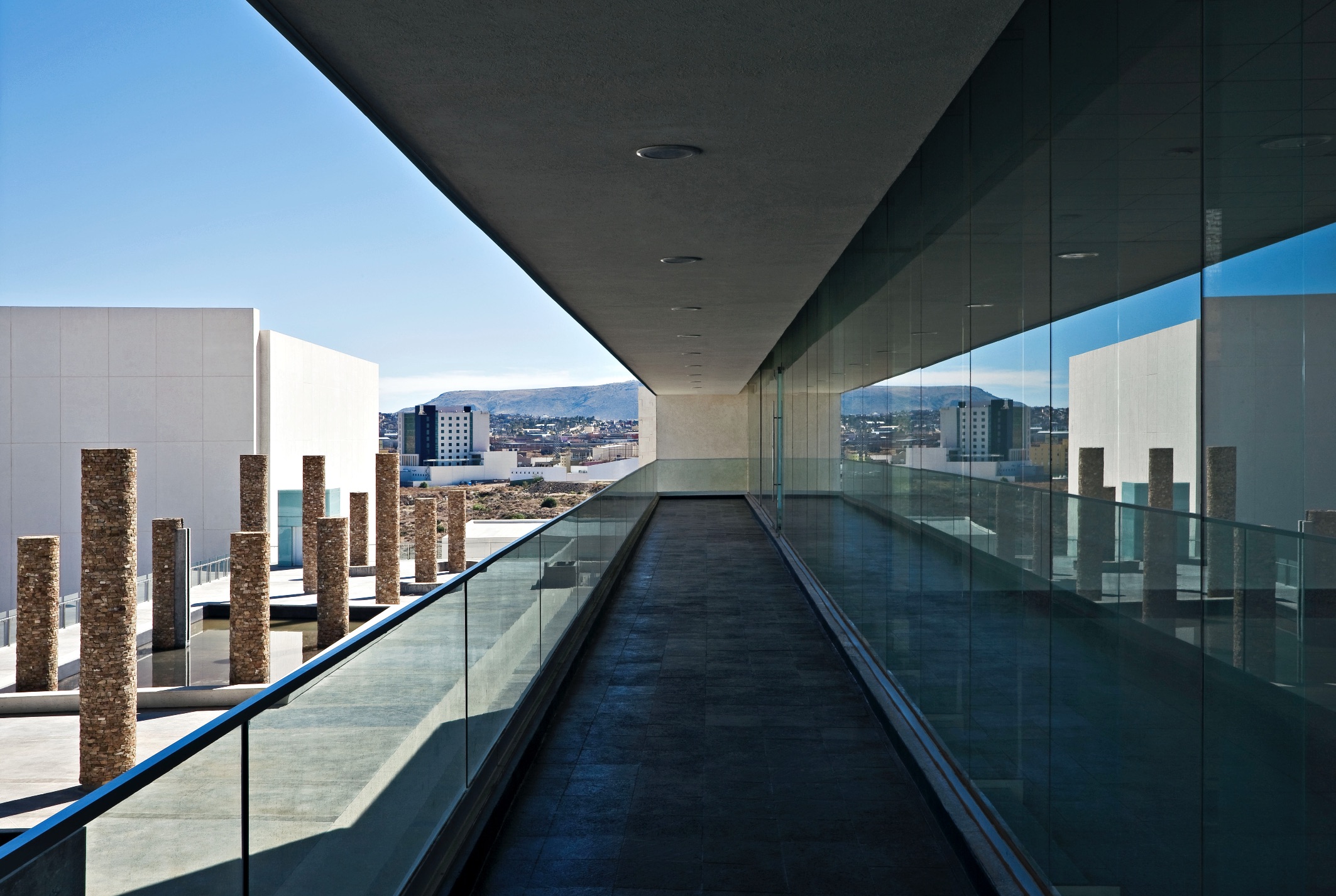 Pasarela exterior con muro de vidrio y columnas de piedra